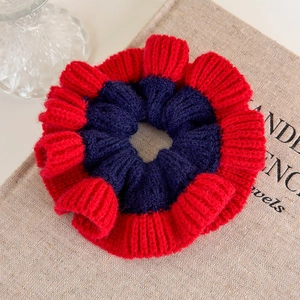 Detail view of red and navy blue knitted scrunchie with soft ribbed texture and elastic design
