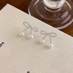 Macro detail of silver bow earrings featuring polished pearls on textured beige card