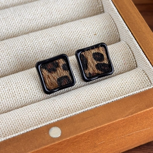 Détail de boucles d'oreilles carrées à motif léopard dans une boîte à bijoux en bois