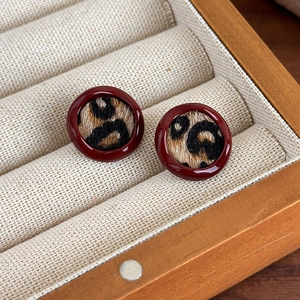 Détail de boucle d'oreille ronde à motif léopard et émail rouge sur présentoir bois
