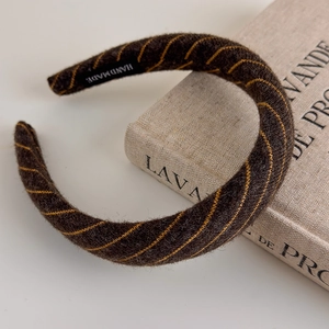 Detailed macro view of deep brown knitted plush headband with yellow stripe texture and hand made label