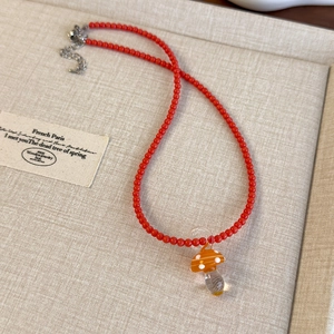 Dettaglio della collana di perle rosse con ciondolo a fungo in vetro arancione