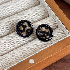 Détail de boucles d'oreilles rondes avec bord noir brillant et texture léopard en poils