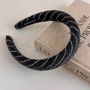 Close-up of black knitted stripe sponge headband with handmade label on beige book
