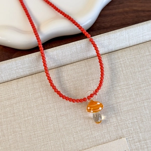 Dettaglio collana di perline rosse con simpatico ciondolo a fungo in vetro arancione