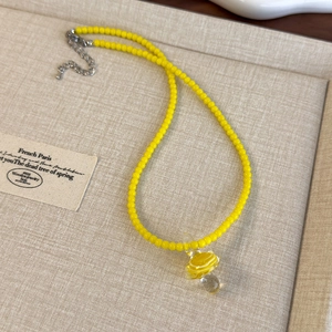 Dettaglio di collana con perline gialle con ciondolo a pianeta e catena di estensione in argento