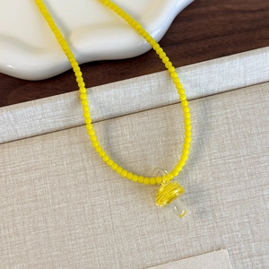 Dettaglio della collana di perline gialle con ciondolo a fungo in vetro su piatto bianco