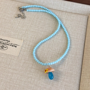 Dettaglio di collana di perline blu con ciondolo a fungo in vetro su vassoio