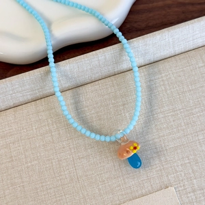 Dettaglio della collana di perline azzurre con ciondolo a forma di fungo in vetro