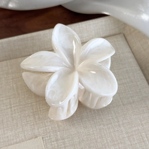 Detailed macro of a pearlescent white flower hair claw clip with a glossy finish