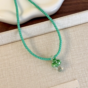 Dettaglio del ciondolo a forma di fungo verde in vetro su una catena di perle colorate