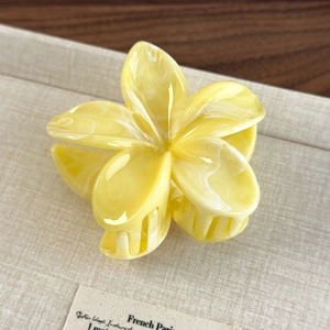 Close-up of yellow marble plumeria claw clip with five-petal flower design on textured paper