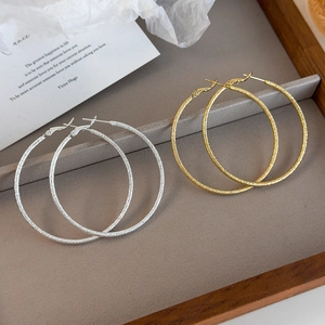 Detailed view of large gold and silver hoop earrings with fine shimmering frosted texture
