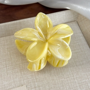 Close-up of yellow flower hair claw with marble texture and pearl luster on a beige tray