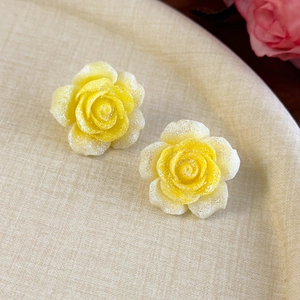 Détail de boucles d'oreilles camélia jaunes avec paillettes sur plateau beige