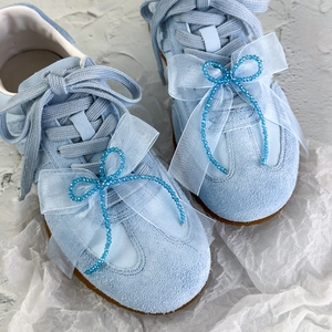 Baskets bleues avec nœuds en organza et perles décoratives sur fond blanc texturé
