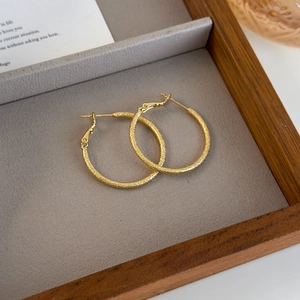 Close-up of golden frosted hoop earrings with a matte textured finish on a felt tray