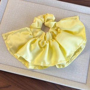 Détail d'un chouchou plissé jaune vif avec une texture soyeuse et un design à volants