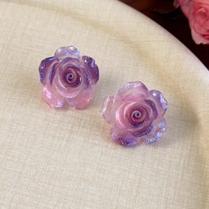 Gros plan de boucles d'oreilles camélia dégradé violet avec une texture de poudre scintillante