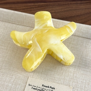 Detail of yellow and white marbled star-shaped hair claw with smooth resin texture