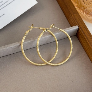 Detailed view of large gold frosted hoop earrings on a velvet display tray with props