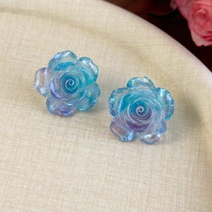 Gros plan de boucles d'oreilles camélia en résine avec dégradé bleu-violet