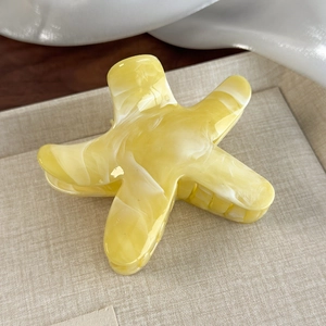 Detailed macro shot of a star-shaped yellow marble hair claw clip on a beige tray