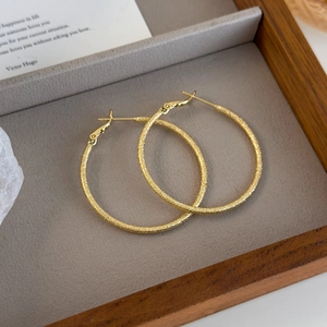 Macro shot of gold hoop earrings with glittery frosted texture on grey leather tray