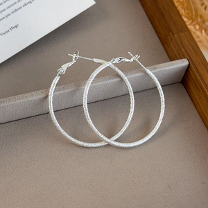 Close-up of large silver glitter textured hoop earrings on a velvet jewelry tray