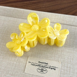 Detail view of yellow acetate floral hair claw with three sunflowers on a beige fabric base