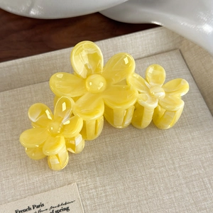 Detail view of yellow marble textured flower hair claw clip on neutral fabric background
