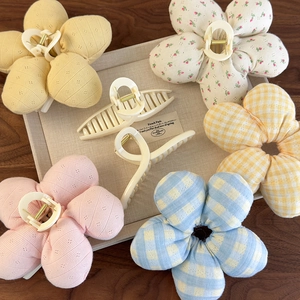 Détail des pinces à cheveux fleurs en tissu et barrettes crème sur plateau texturé
