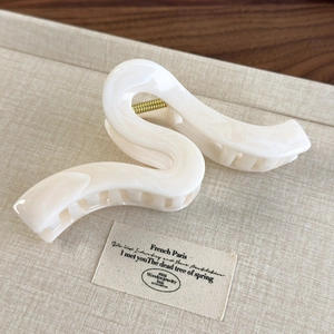 Detailed close-up of a wavy cream-white hair claw clip with golden metal spring