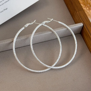 Detail of large silver hoop earrings featuring a sparkling frosted matte texture finish
