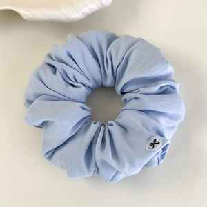 Vue détaillée du chouchou à carreaux bleu clair avec mini emblème de nœud papillon