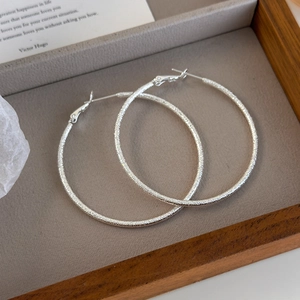 Macro shot of silver textured hoop earrings with sparkling frosted finish on a gray tray