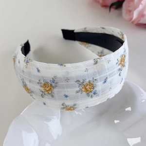 Détail d'un large serre-tête floral avec roses jaunes et fleurs bleues sur tissu