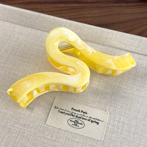 Macro detail of S-shaped marble pattern hair claw with lemon yellow acetate and gold spring