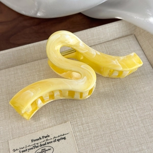 Detailed macro view of a large yellow marble acetate hair claw clip with golden metal spring