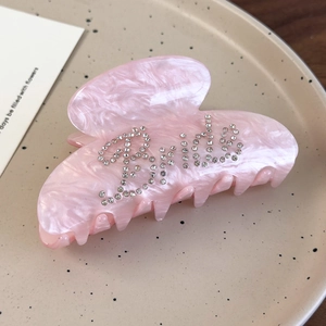 Macro detail of pink acetate hair claw clip with rhinestones spelling Bride lettering