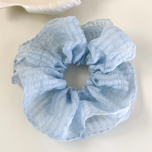 Détail d'un chouchou à carreaux bleu clair avec fils pailletés sur un plateau blanc
