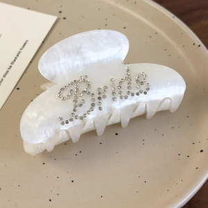 Detail of pearlescent hair claw clip with rhinestones spelling Bride on a ceramic plate