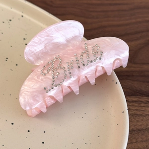 Macro detail of pink marble hair claw clip with crystal Bride lettering on ceramic plate