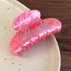 Detail of pink marble acetate hair claw clip with Girl rhinestone lettering on a ceramic plate