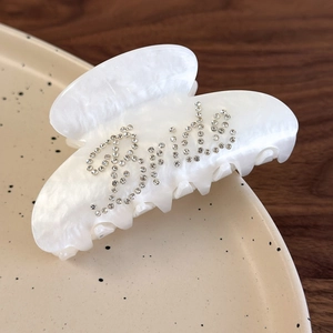 Detailed view of pearl white hair claw clip with silver rhinestone Bride text decoration