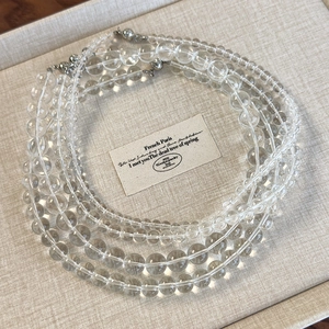 Minimalist transparent acrylic beaded choker necklaces set on cream fabric background