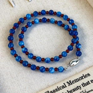 Blue marble and red garnet beaded necklace with silver buckle on beige linen