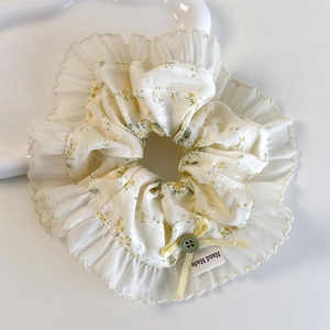 Détail d'un chouchou floral jaune avec bordure en dentelle, bouton et étiquette faite main