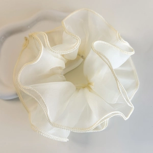 Vue rapprochée d'un chouchou en organza blanc crème sur un plateau en céramique ondulé