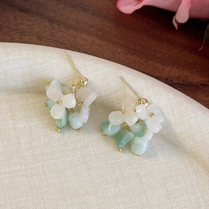 Gros plan de boucles d'oreilles en forme de fleur menthe et blanche, détails dorés
